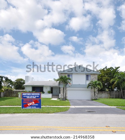 Sold (Another Success let us help you buy sell your next home) Real Estate Sign on front yard of Suburban Back Split style home residential neighborhood USA blue sky clouds