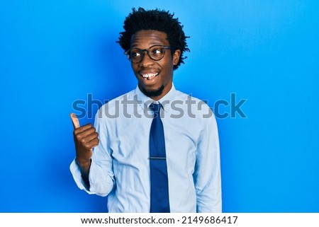 Young african american man wearing business clothes pointing thumb up to the side smiling happy with open mouth 