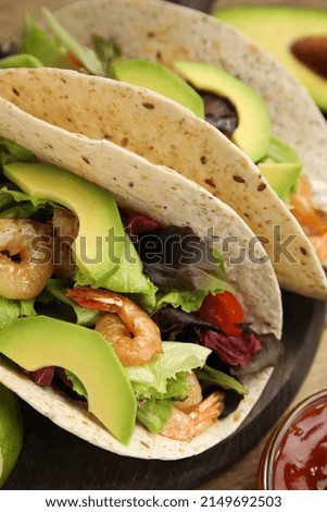 Delicious tacos with shrimps and avocado on table, closeup