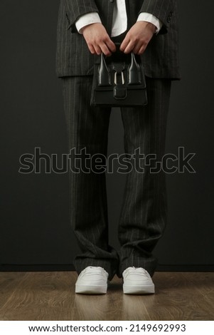 Fashionable trendy woman holding top handle mini black bag. Studio shot on black background.