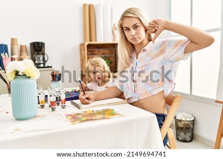 Caucasian family of mother and daughter painting at art studio with angry face, negative sign showing dislike with thumbs down, rejection concept 