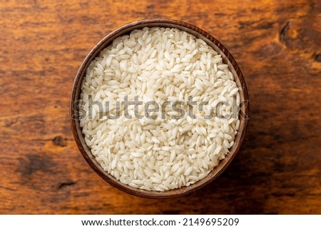 Uncooked Carnaroli risotto rice in bowl on a wooden table. Top view.