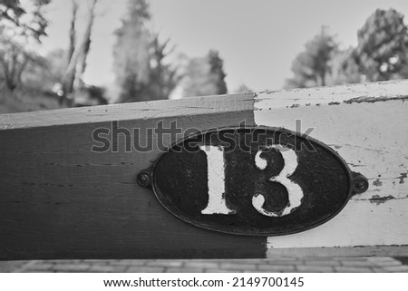 An old metal plate fixed on a wooden beam with the numerals 13 embossed on it photographed in black and white