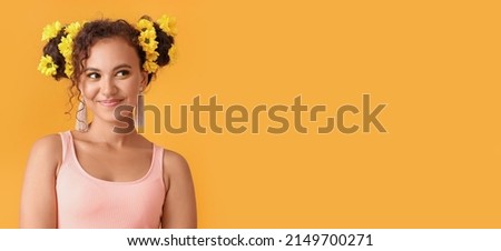 Happy young African-American woman with flowers in her hair on orange background with space for text