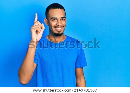 Young african american man wearing casual blue t shirt pointing finger up with successful idea. exited and happy. number one.  Royalty-Free Stock Photo #2149701387