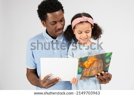 Portrait of little African-American girl and her father reading book on grey background
