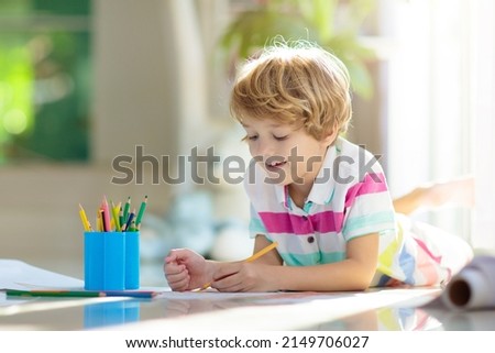 Child drawing lying on the floor. Kid painting rainbow. Online remote learning arts and crafts homework for school kids. Little boy with colorful pencils. Children draw. Creativity and imagination fun