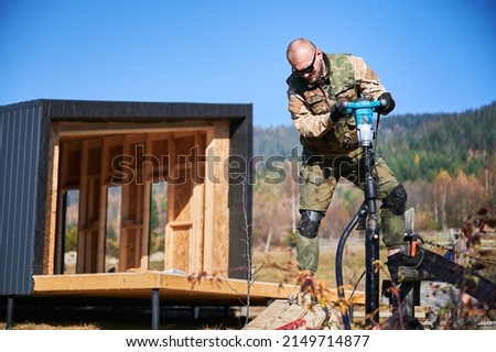 Male workers building pile foundation for wooden frame house. Men builders drilling piles into the ground on blue sky background. Royalty-Free Stock Photo #2149714877