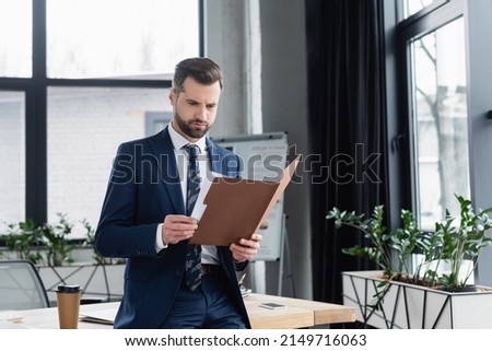 economist looking in folder while standing near desk in office Royalty-Free Stock Photo #2149716063