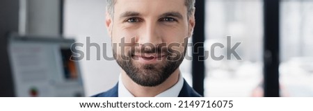 portrait of happy bearded economist smiling at camera in blurred office, banner