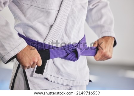Ready to fight. Cropped shot of an unrecognizable man tying a purple belt around hist waist while in full jiu jitsu gi. Royalty-Free Stock Photo #2149716559