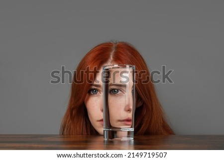 distorted face of woman looking through glass of water - introspection and duality concept with creative refraction