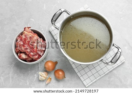 Pot with delicious bone broth and ingredients on light grey table, flat lay