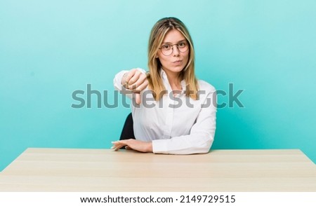 pretty blonde woman feeling cross,showing thumbs down. business and desk concept