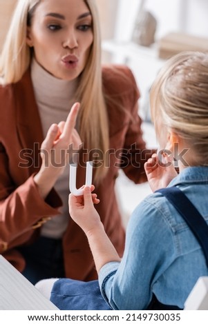 Blurred child holding letter near speech therapist gesturing in consulting room Royalty-Free Stock Photo #2149730035