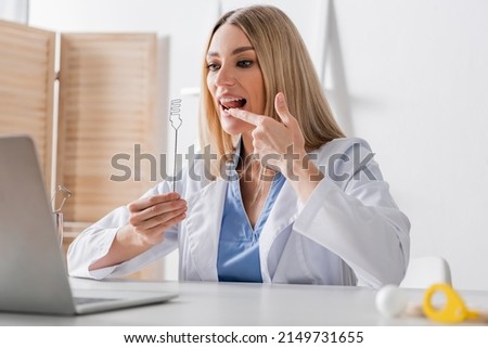 Speech therapist holding tool and pointing at mouth during video call on laptop Royalty-Free Stock Photo #2149731655