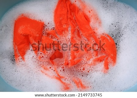 Orange garment in suds, top view. Hand washing laundry
