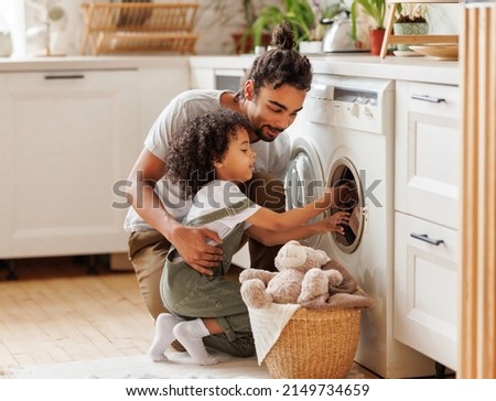 Cheerful black kid boy helping father at linen in basket while doing laundry near washing machine in flight kitchen in weekend at home   Royalty-Free Stock Photo #2149734659