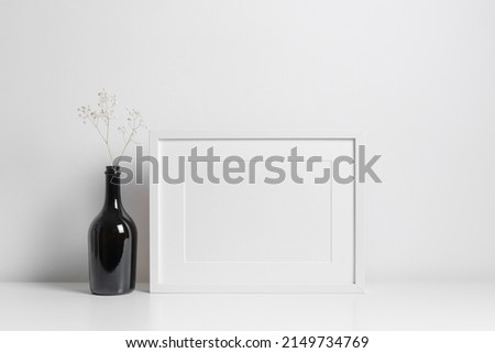 Horizontal frame mockup in white minimalistic interior with dark bottle decorations