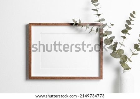 Wooden frame mockup on white wall with copy space for artwork, photo or print presentation in minimalistic interior with eucalyptus twig.