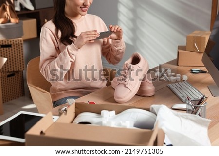 Shoes seller taking picture of pink sneakers at table in office, closeup. Online store