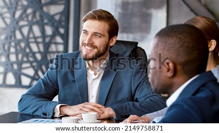 Young man in a suit listening to a corporate leader at a meeting with a team