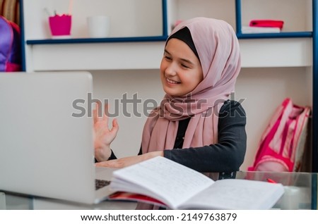 Smiling Muslim student girl in hijab wave greeting with teacher tutor while study online on laptop at home desk. 