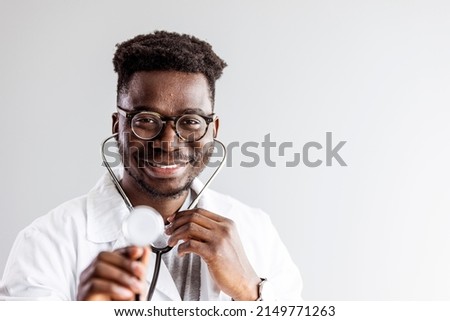 Medical concept of young male doctor in white coat with phonendoscope, waist up. Man hospital worker looking at camera and smiling, studio, grey background. Friendly african male therapist 