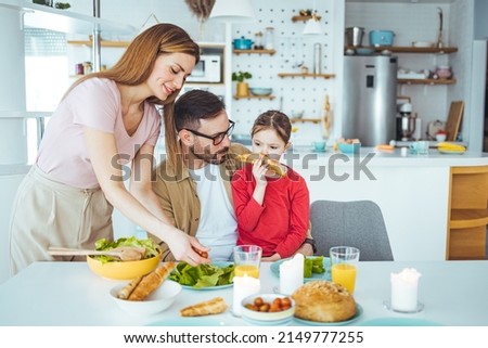 Mom, dad and daughter cook in the kitchen. The concept of a happy family. A handsome man, attractive young women and their sweet daughter eat salad and bread together. Healthy way of living.