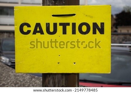 Caution sign in black letters on a yellow background fixed to a wooden telephone pole