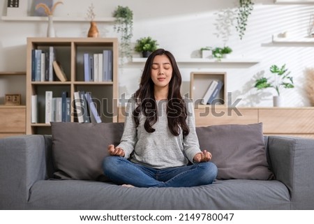 Clam of Asian young woman doing yoga lotus pose to meditation and relax on couch during work online at home.Happiness female break after worked close her eyes and deep breath with yoga so peaceful. Royalty-Free Stock Photo #2149780047