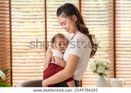 Asian mom holding her baby newborn in hand and kissing baby sweet and lovely.Good moment of Happy mother and infant baby looking together smile with love.Mother and baby newborn Concept