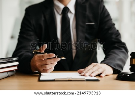 A lawyer sits in his office, on a table with a small hammer to beat the judges desk in court. and justice scales, lawyers are drafting a contract for the client to use with the defendant to sign. Royalty-Free Stock Photo #2149793913