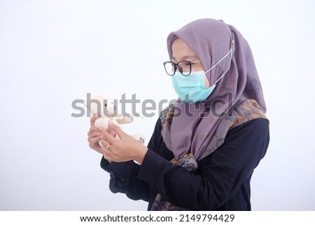 Muslim woman wearing a mask carrying a teddy bear