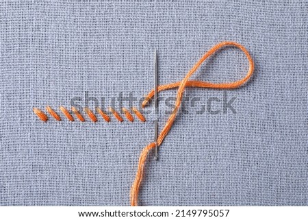 Needle with orange embroidery floss and row of stitches on grey fabric, top view Royalty-Free Stock Photo #2149795057