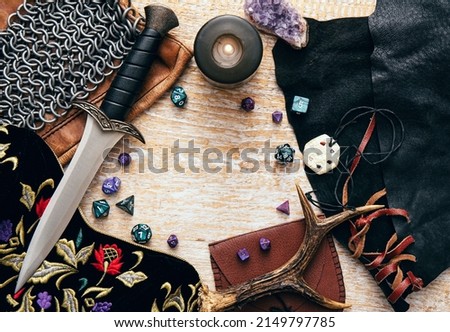 Fantasy role play board game concept. Frame decorated with various character objects tools with copy space. Dagger, chain mail, amulet, clothing, dice set: D10, D20, D12, D6, D8. Royalty-Free Stock Photo #2149797785