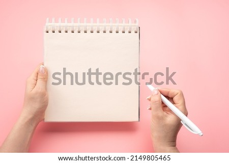 writing in blank notepad on pink background. Mockup notepad. woman hand with pen next to an empty blank notepad. top view of hand holding pen against spiral notepad on pink table, taking notes concept Royalty-Free Stock Photo #2149805465