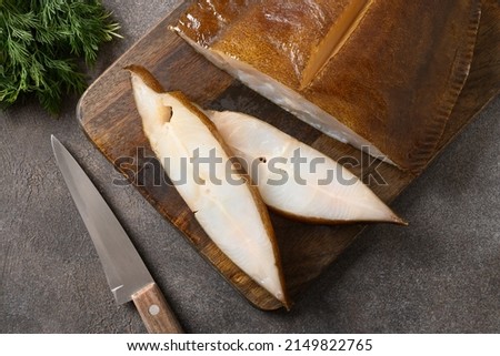 Smoked halibut slices on cutting wooden board on brown background. View from above. Cold appetizer of healthy white fish with omega 3.