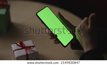 old female hands holding smartphone with green screen and celebrating holiday chatting with family, wide photo