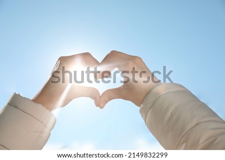 Woman showing heart against blue sky outdoors on sunny day, closeup of hands
