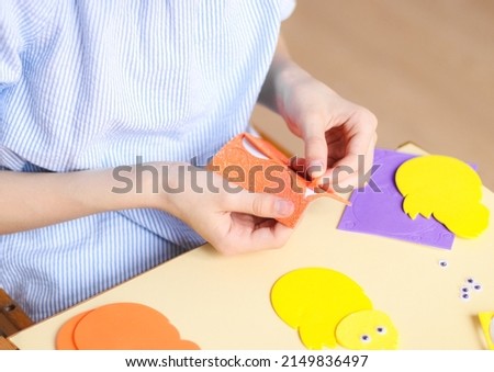 The hand of a Caucasian teenage girl peels off a sticker from an orange felt to stick to a yellow felt chicken