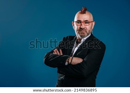portrait of punk-style businessman looks at camera in studio shot with his arms crossed and expression of confidence on blue background