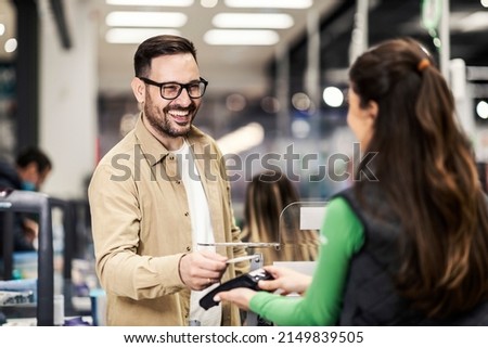 A smiling customer using credit card in supermarket at checkout.