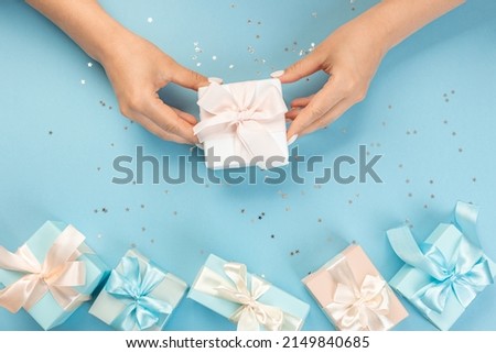 Flat lay of women's hands holding a gift wrapped and decorated with a bow on a blue background with silver sequins with copy space
part of the table is surrounded by several festively wrapped gifts