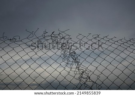 Wire fence or metal net on sunset background, blue sky. hole in net.