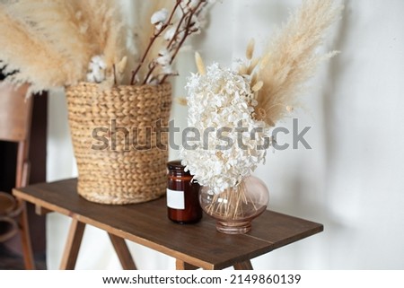 Cozy autumn decor room: on wooden table wicker basket with dried flowers, candle and vase with pampas grass. Vase with bouquet of dried hydrangea, spikelets, ears and plants. living room interior 
