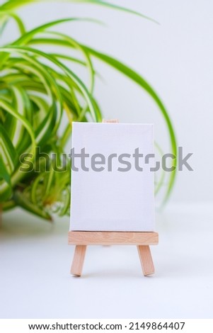 Minimalistic simple natural light mock up template. Empty space for text, logo, design. Stand for booklets, invitation, label with white paper, wooden tent card. Potted Chlorophytum comosum in a frame