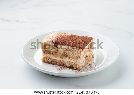 Piece of Homemade Tiramisu cake dessert on a white marble background
