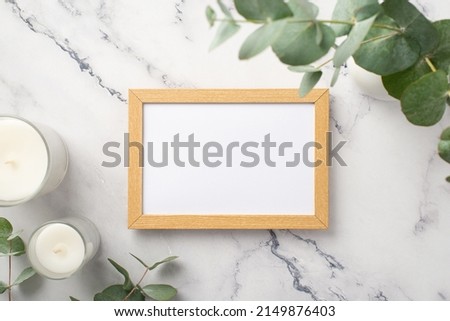 Top view photo of wooden photo frame candles and eucalyptus on white marble background with empty space