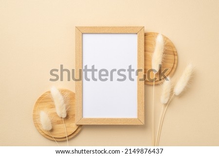 Top view photo of wooden photo frame and white lagurus flowers on wooden stands on isolated beige background with empty space